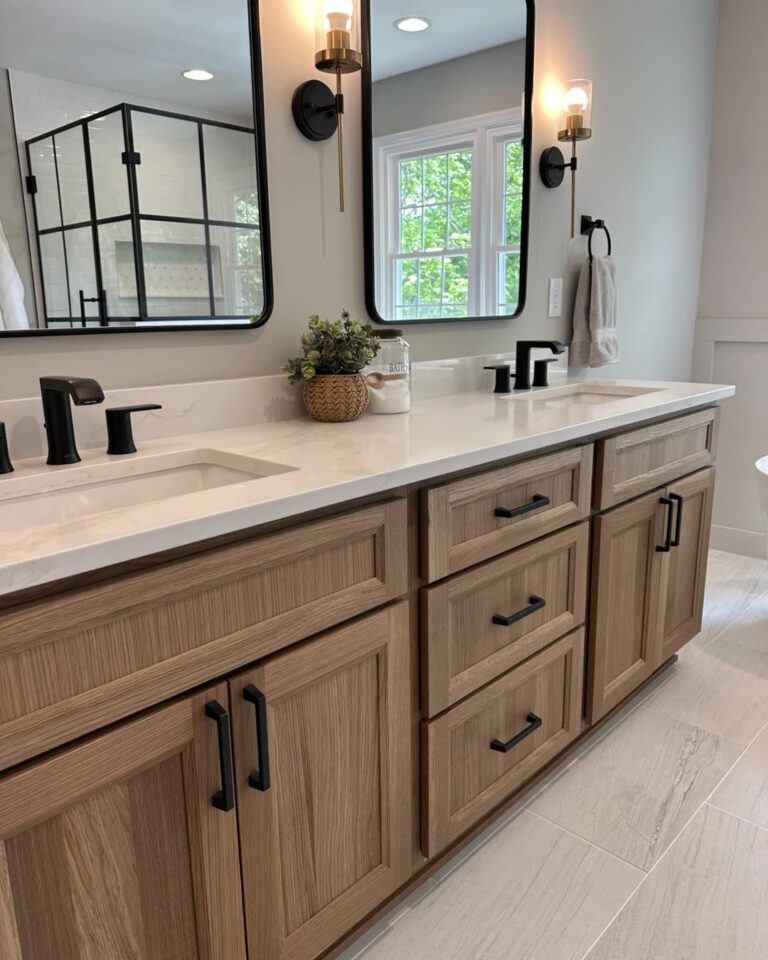 Custom bathroom renovation featuring a warm wood double vanity, matte black plumbing fixtures, quartz countertops, modern sconces, and black framed mirrors by Central Maryland interior design studio Grit & Ash Designs.