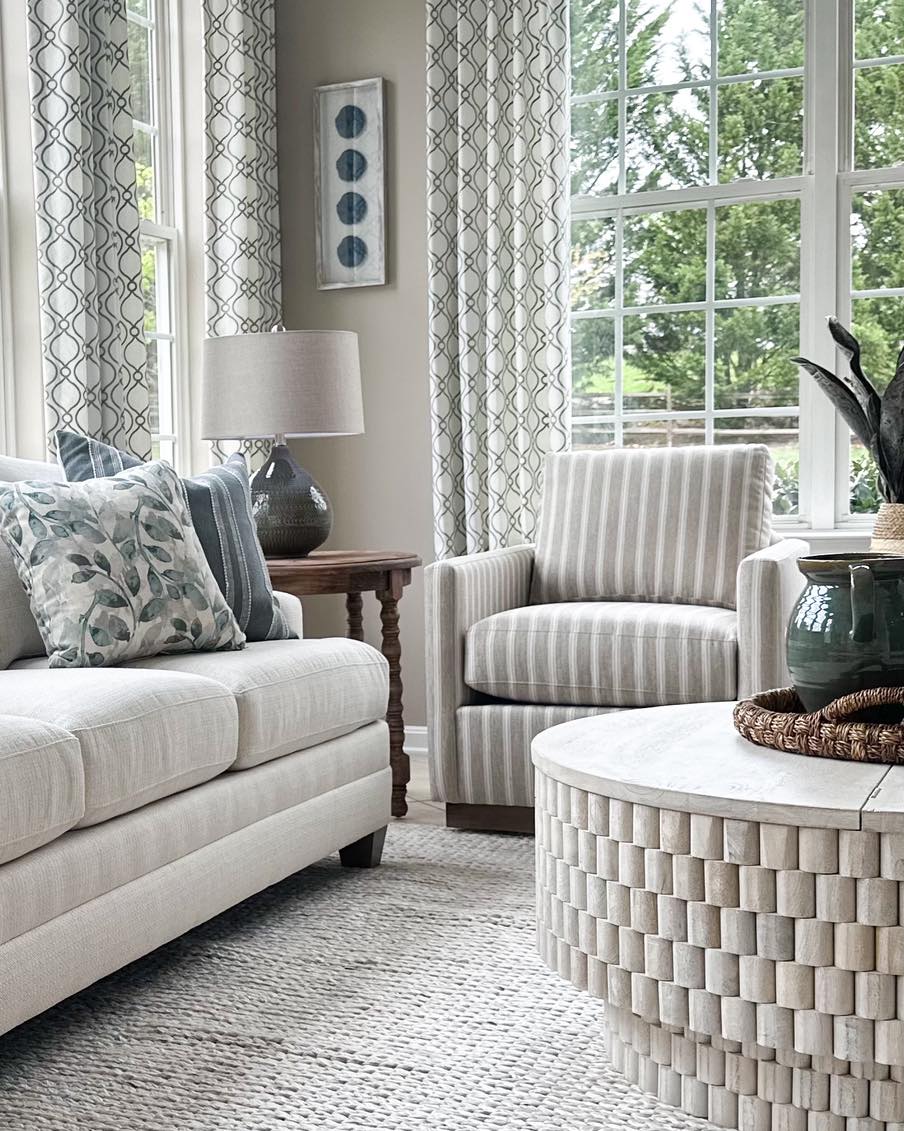 Neutral living room interior design featuring layered textures, patterned drapery panels, striped accent chair, woven coffee table, and soft blue and green accents by Central Maryland interior design studio Grit & Ash Designs.