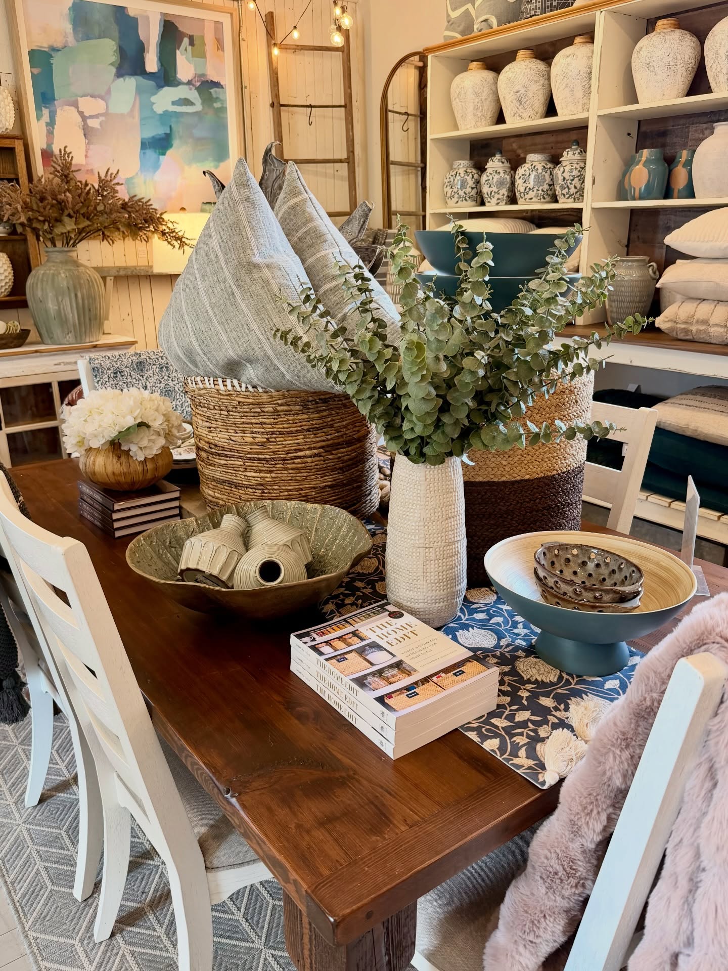 Styled dining table display inside Grit & Ash Designs featuring vintage-inspired home décor, woven baskets, decorative pottery, eucalyptus stems, and neutral-toned accessories in Glenwood, Maryland.
